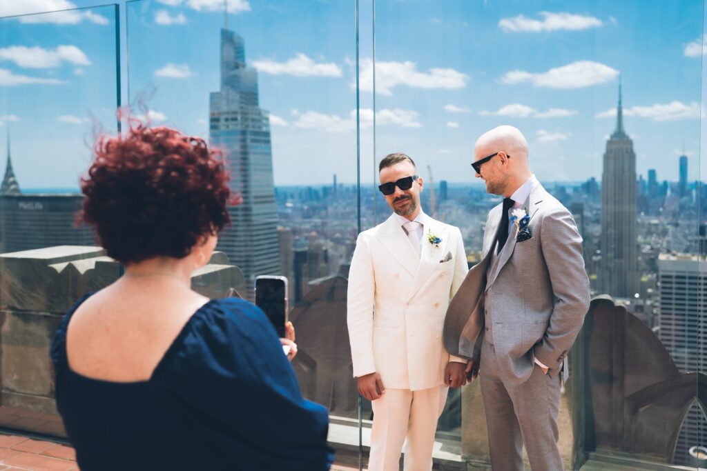 Two grooms getting married at the Top of the Rock rooftop with Manhattan skyline, officiated by Jackie Reinking