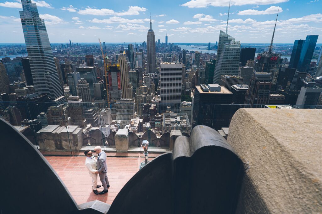 Wide-angle photo of Top of the Rock rooftop with couple and Manhattan skyline, officiated by Jackie Reinking.