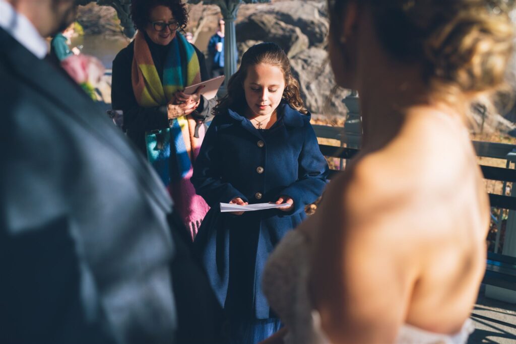 Madeleine and Craig’s daughter reading during their Central Park ceremony at the Ladies Pavilion, with officiant Jackie Reinking